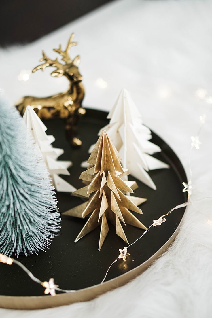 three christmas trees are sitting on a black platter with white and gold decorations around them