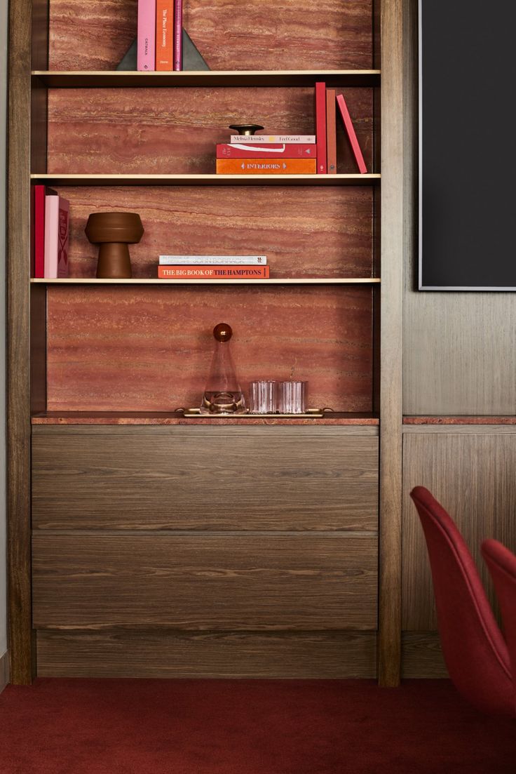 a book shelf with books on it and a red chair next to it in front of a flat screen tv