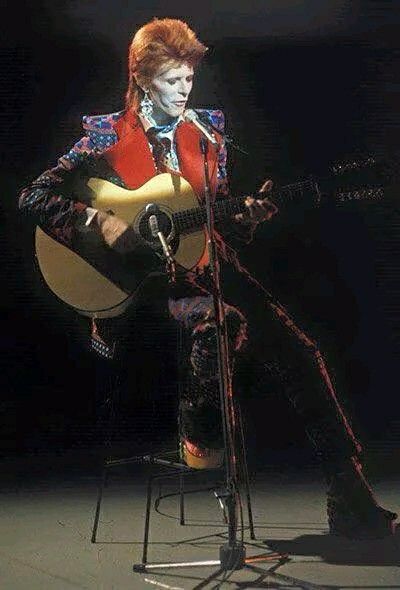 a man sitting on top of a chair holding a guitar in front of a microphone