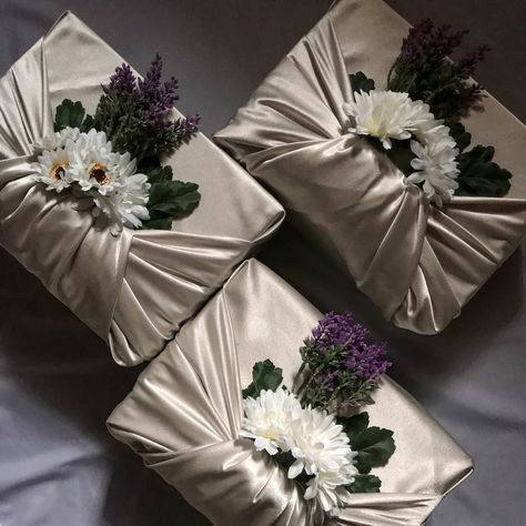 three boxes with flowers on them sitting on a bed next to each other and one is wrapped in satin material