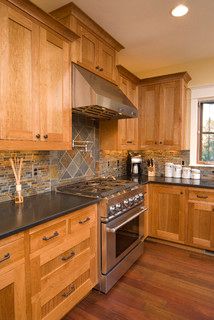 a kitchen with wooden cabinets and black counter tops, stainless steel appliances and wood flooring