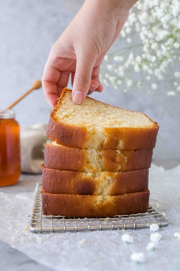 a person is picking up a piece of cake from a cooling rack with honey in the background