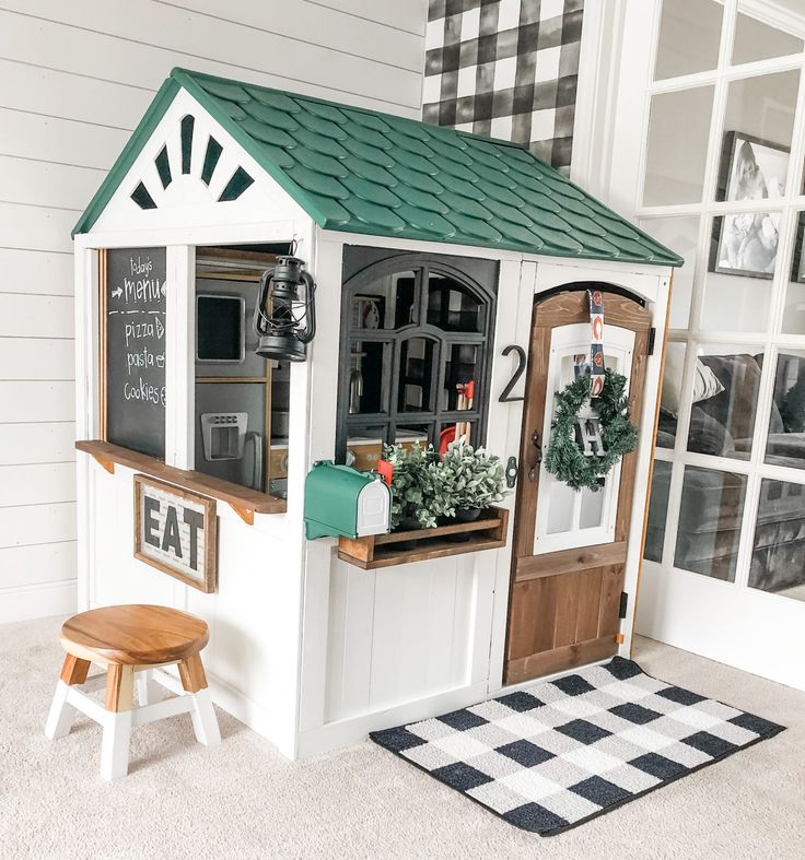 a dollhouse with a green roof and white walls, sitting on the floor next to a black and white checkered rug