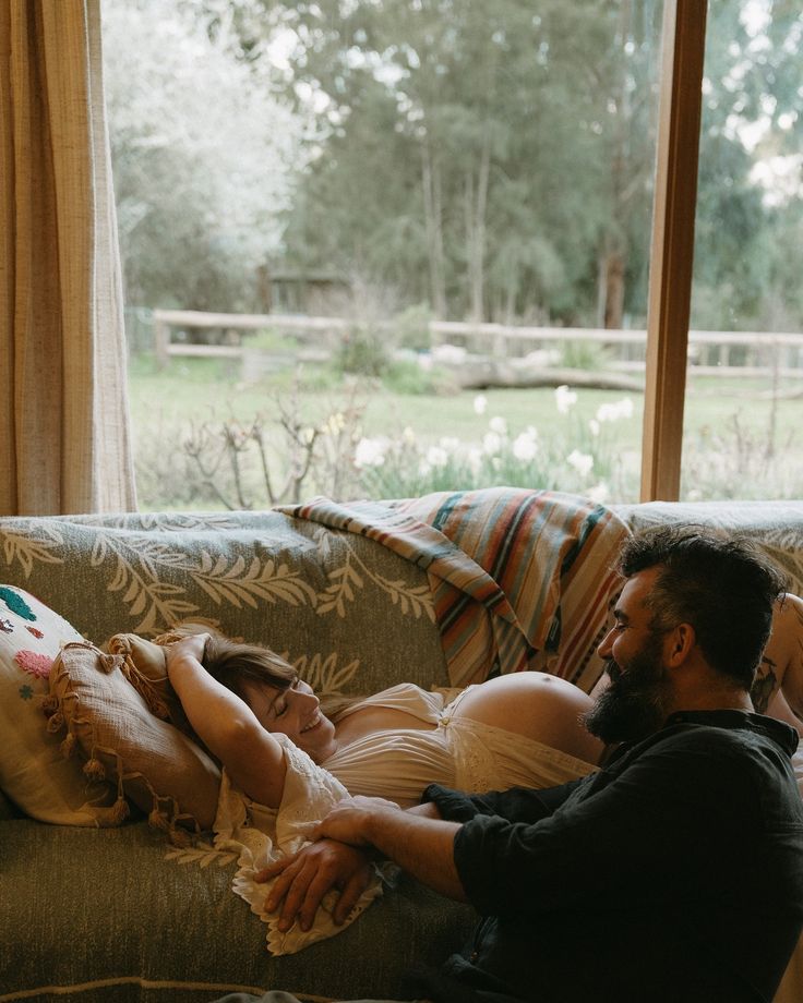 a man and woman laying on a couch in front of a window looking at each other