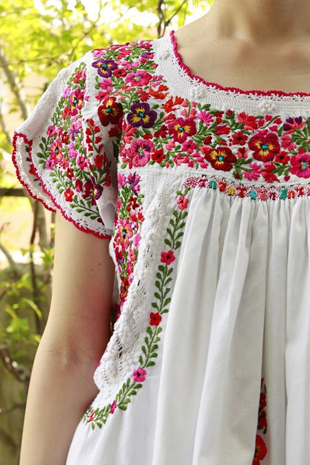 a woman wearing a white dress with red and green flowers on it's chest