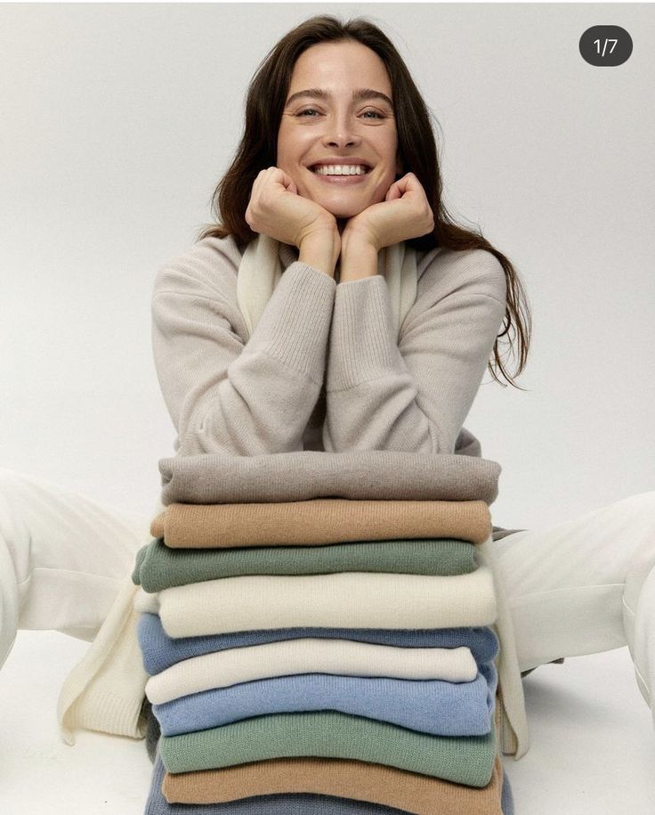 a woman sitting on the ground with her arms crossed and folded up in front of stacks of sweaters