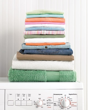 a stack of folded towels on top of a white shelf next to a pile of folded clothes