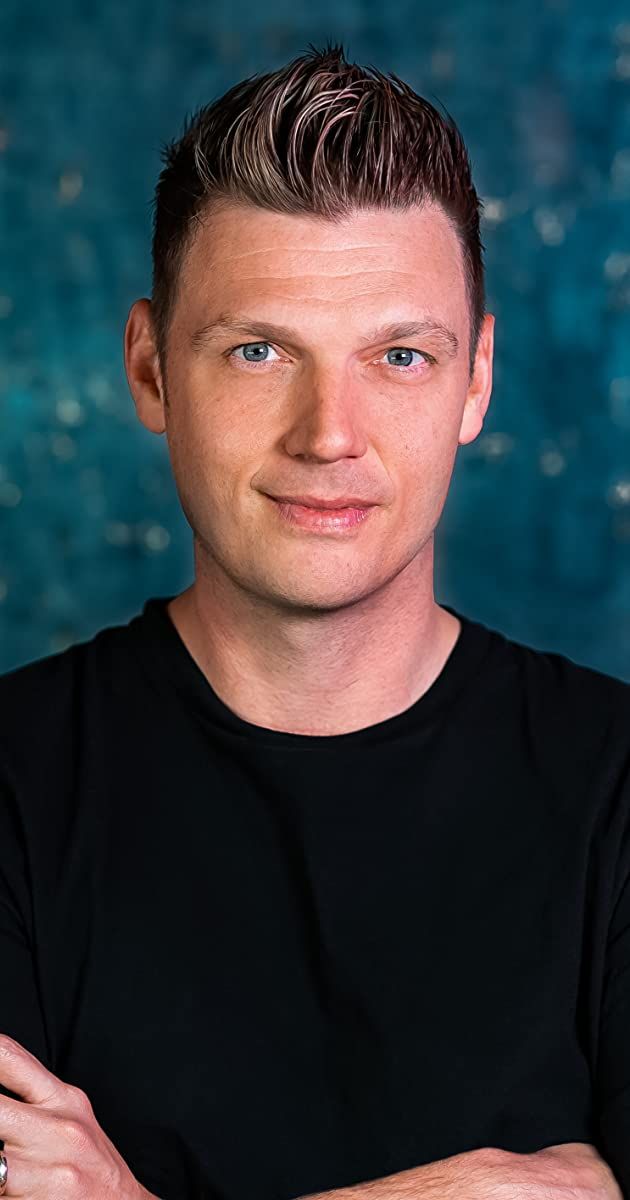 a man with his arms crossed in front of a blue wall and water behind him