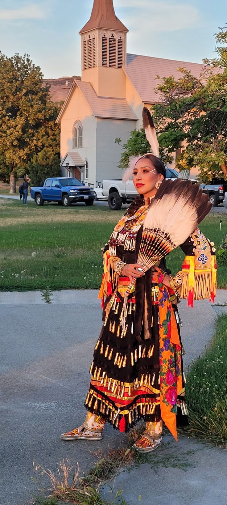 a woman dressed in native clothing standing on the side of a road next to a church