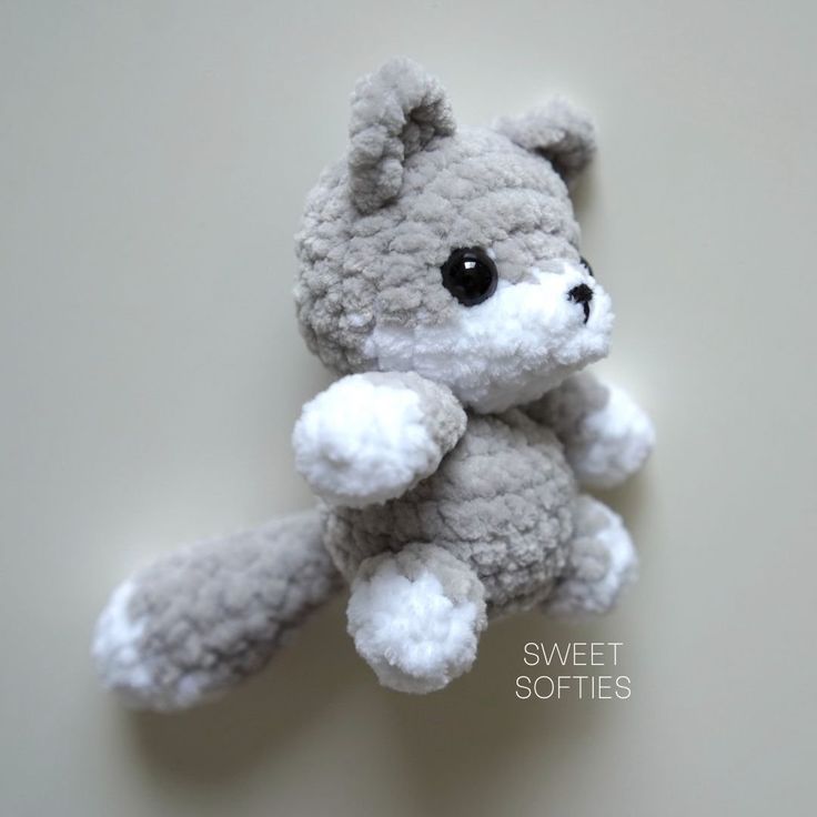 a small gray teddy bear sitting on top of a white table next to a wall