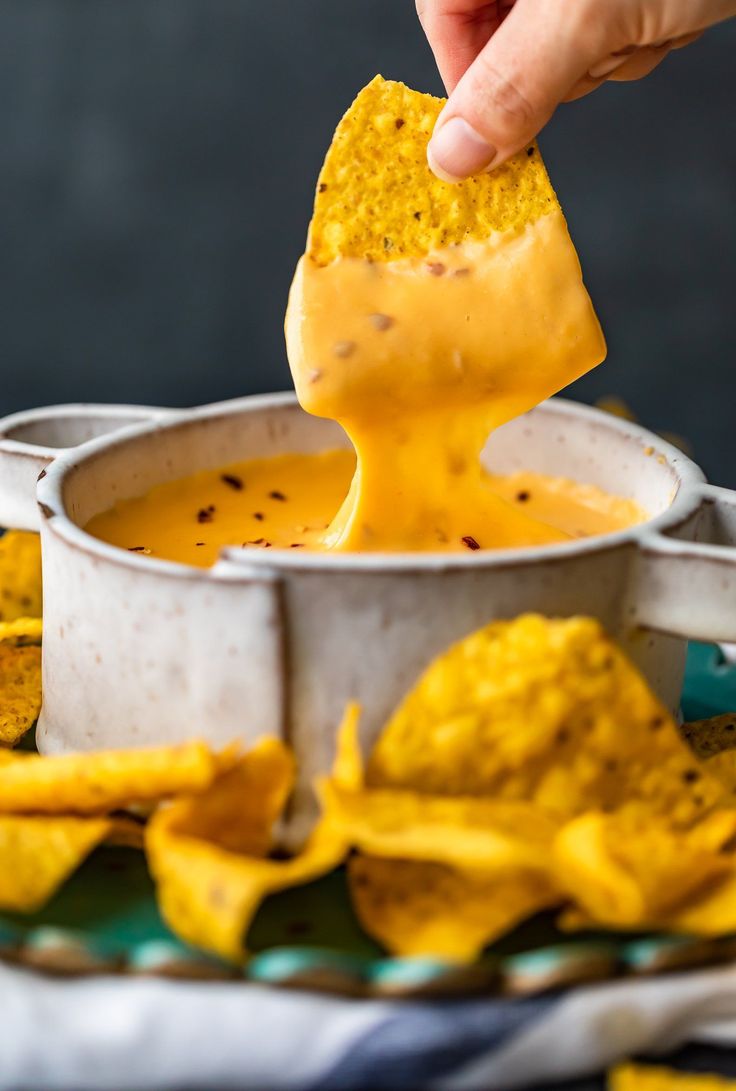 a person dipping cheese into a bowl of tortilla chips