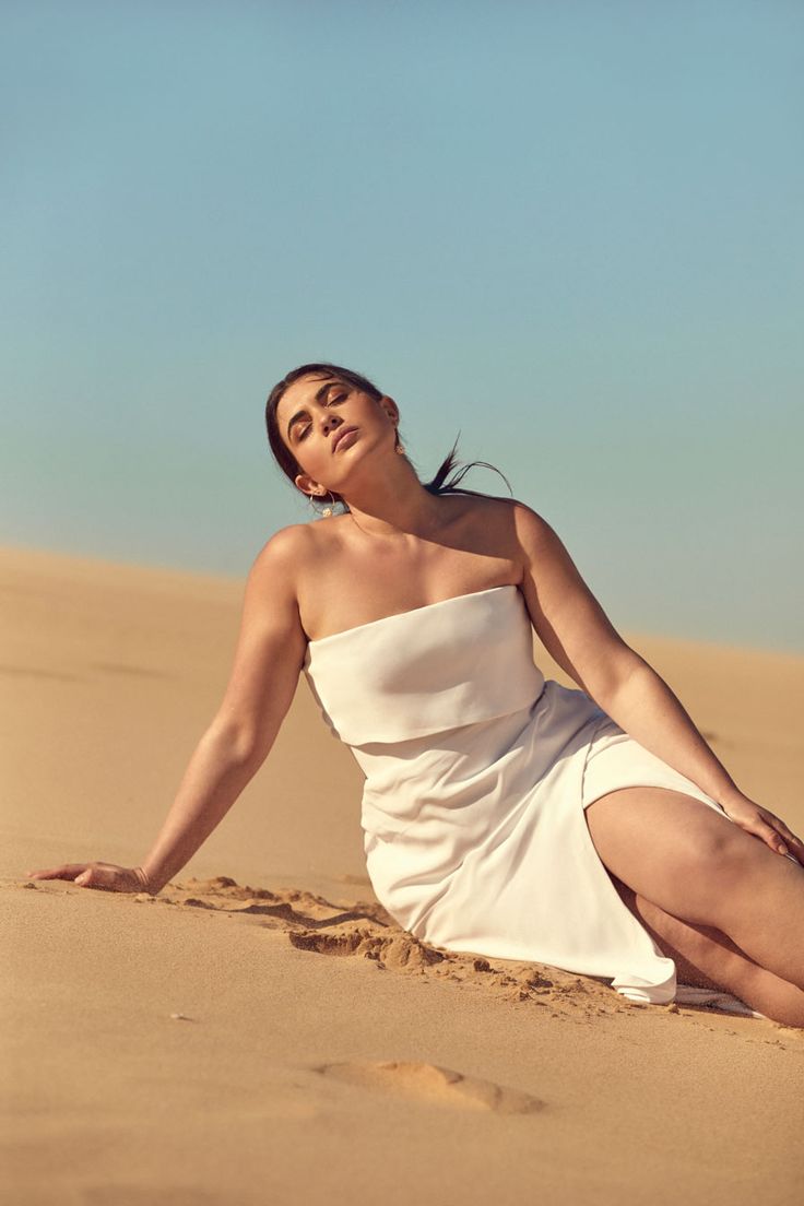 a woman in a white dress sitting on the sand