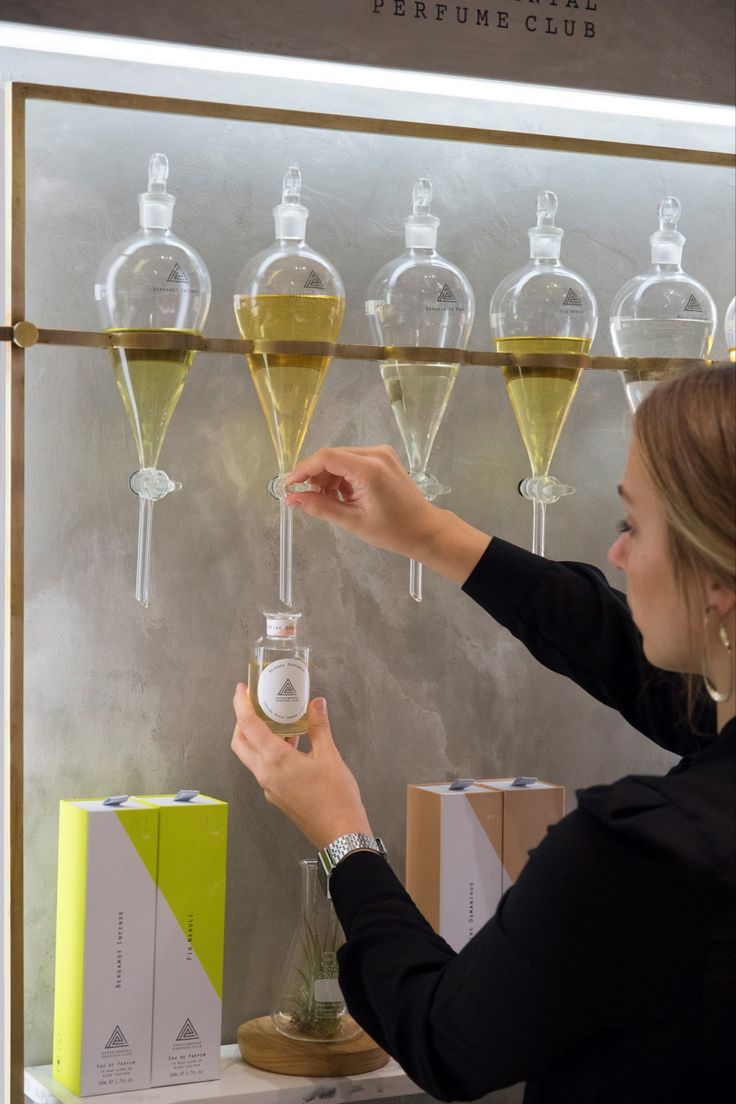 a woman is pouring some liquid into wine glasses in front of a wall with bottles on it