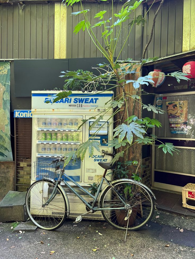 a bicycle parked next to a vending machine with plants growing out of the front