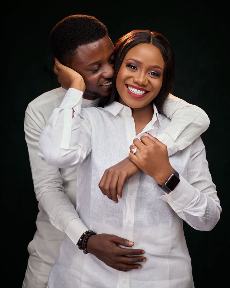 a man and woman embracing each other while they pose for a photo in front of a black background