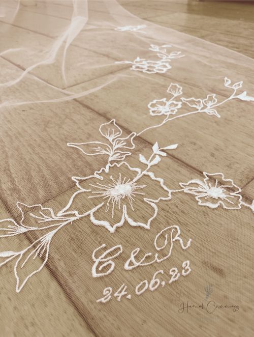 a wedding veil with flowers on it laying on top of a wooden floor in front of a window