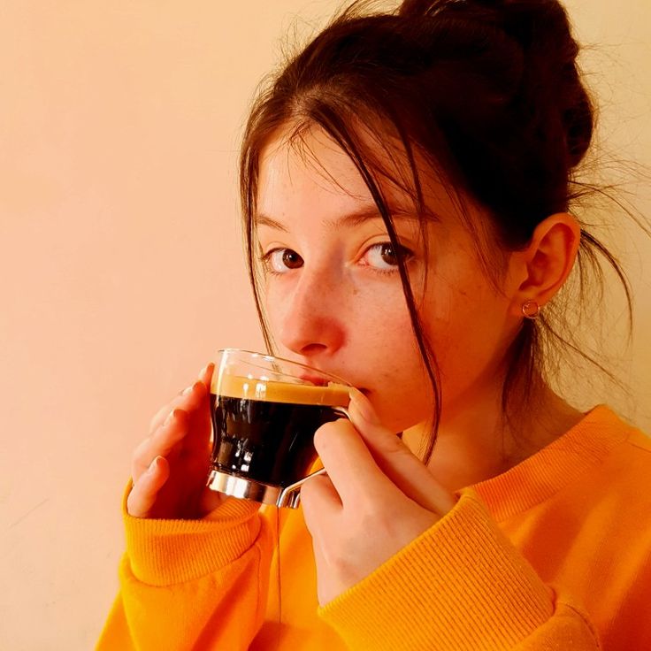 a woman in an orange sweater drinking from a cup