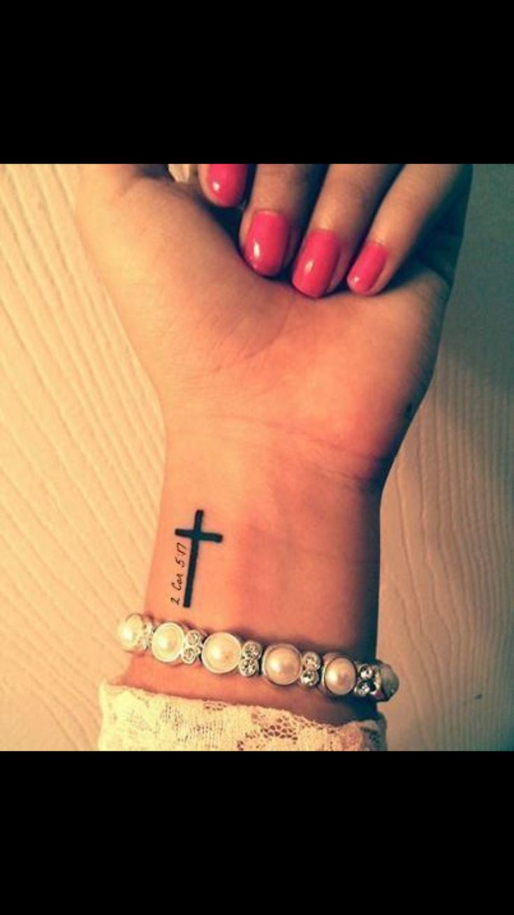 a woman's wrist with a cross tattoo on it and pearls around the wrist