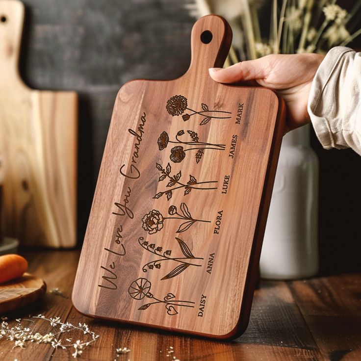 a person holding a wooden cutting board with flowers on it and writing on the side