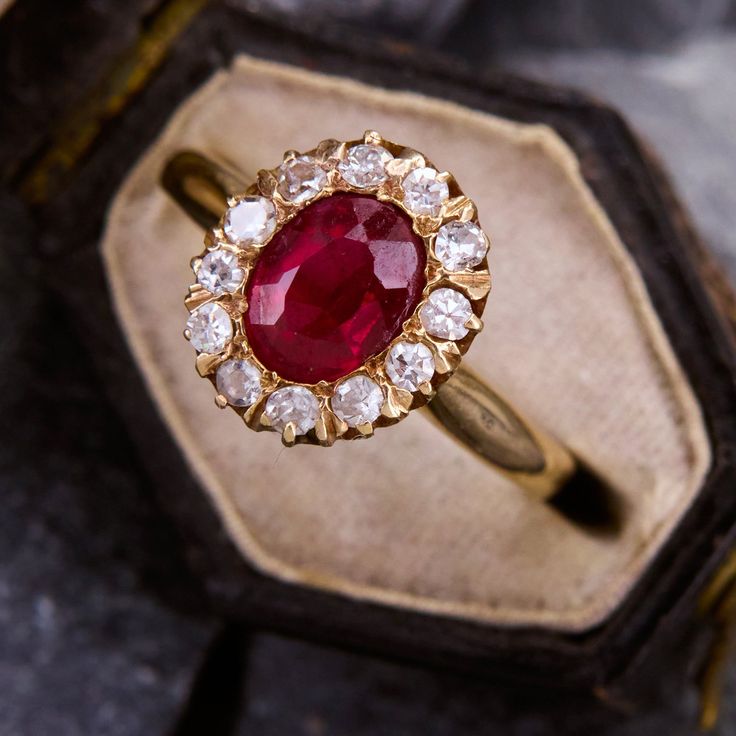 an antique ring with a red stone surrounded by white and yellow diamonds in a wooden box