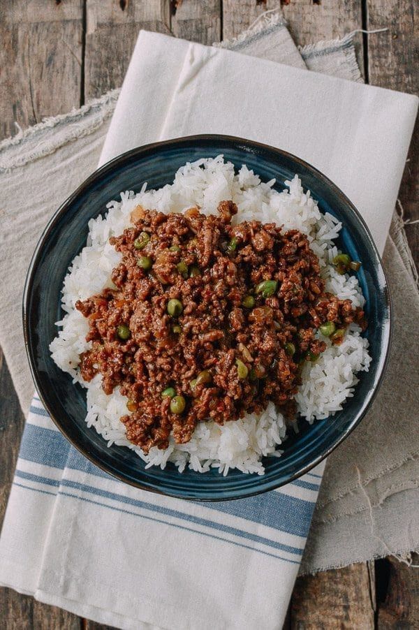 a blue plate topped with rice and ground beef on top of a wooden table next to a napkin