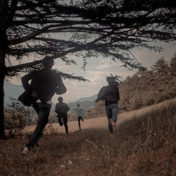 three people are running up a hill in the dark with trees and mountains behind them