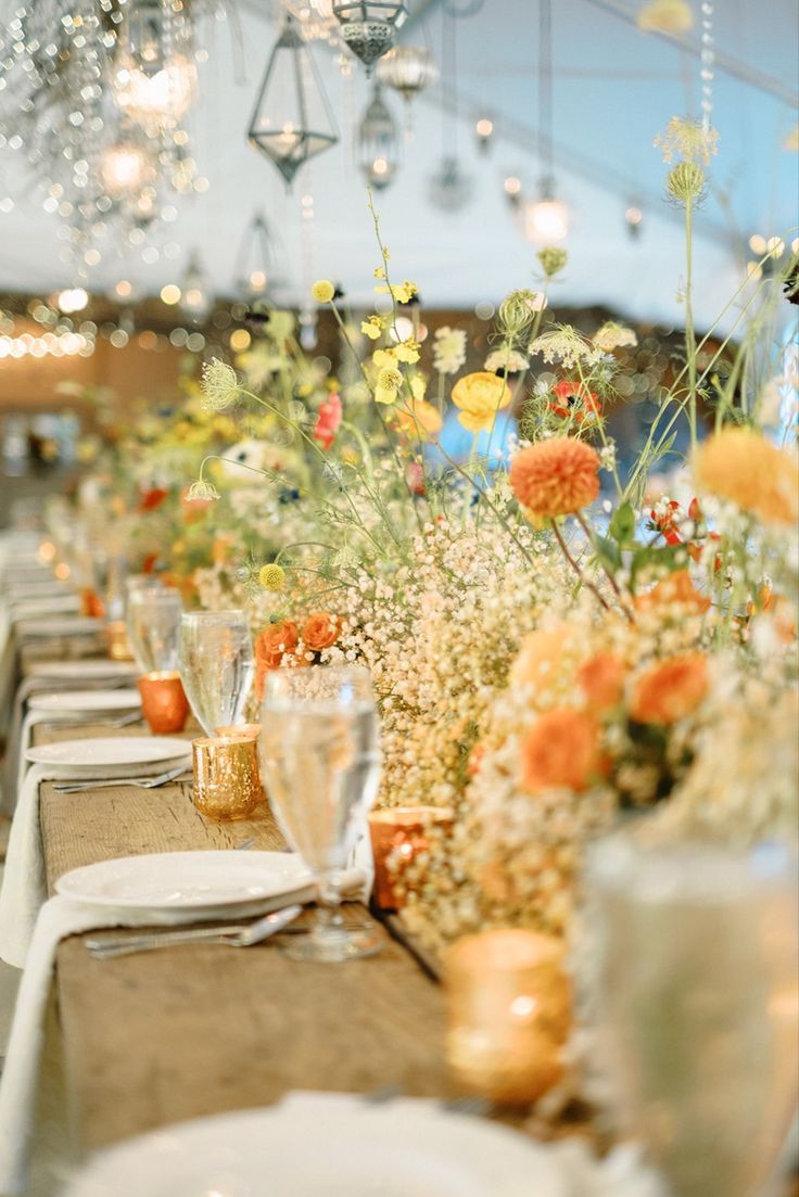 A head table at a wedding reception decorated with baby's breath down the entire 25 foot table with dahlias, ranunculus, roses, anemones, and wild flowers poking out of it. All with a color scheme of orange, peach, yellow, red, and dark purple. Designed by the florists at Camrose Hill. Camrose Hill is an outdoor wedding venue and florist located in Stillwater, Minnesota. Classy Elegant Wedding Dress, Wedding Decor Reception, Classy Elegant Wedding, Orange Wedding Decorations, Yellow Wedding Decorations, Summer Wedding Venues, Wildflower Centerpieces, Stillwater Minnesota, Dahlias Wedding