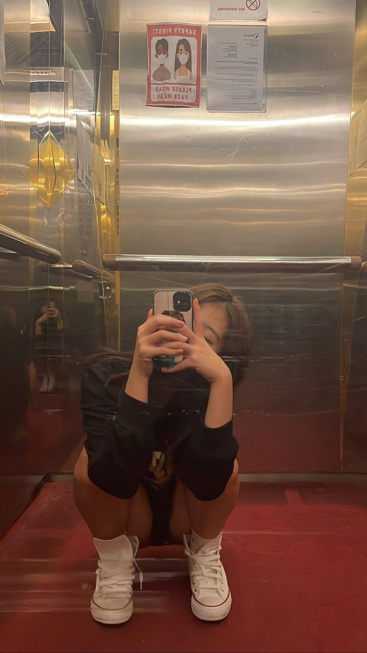 a woman taking a selfie in front of a metallic wall with red carpeting