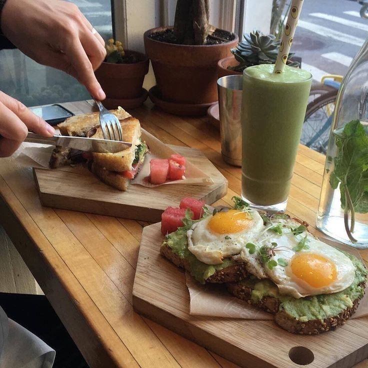 a person cutting up food on top of a wooden cutting board next to a green smoothie