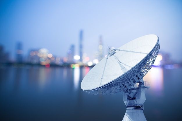 a satellite dish sitting on top of a metal pole in front of a city skyline