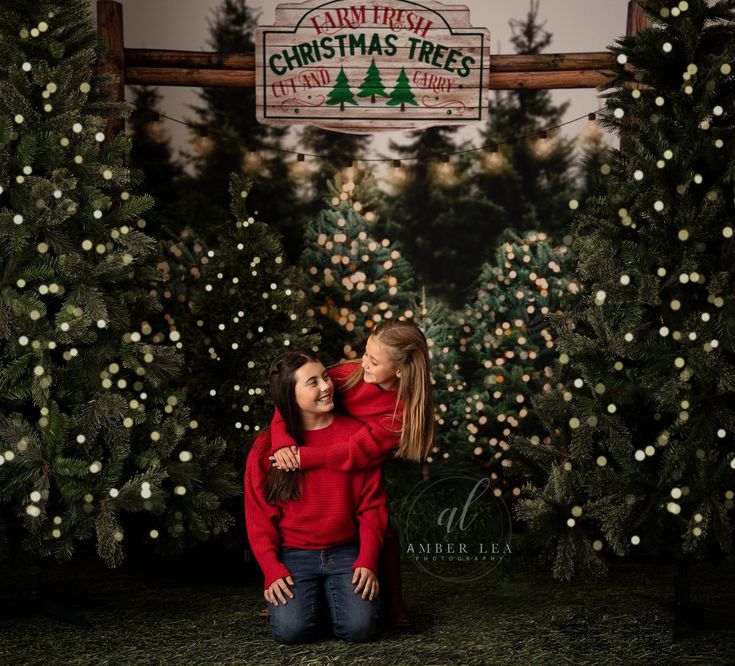 two girls hugging each other in front of christmas trees at an outdoor tree farm with lights