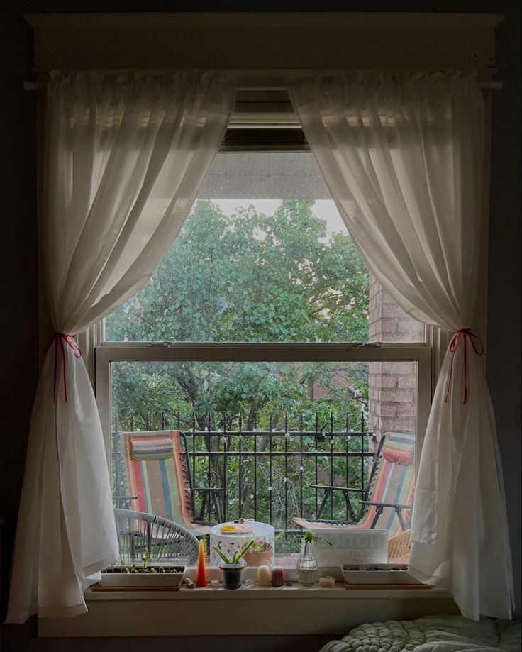 an open window with curtains on the outside and patio furniture in the inside, behind it