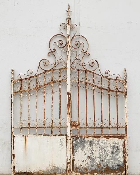 an old iron gate with rusted paint on the outside and inside, against a white wall