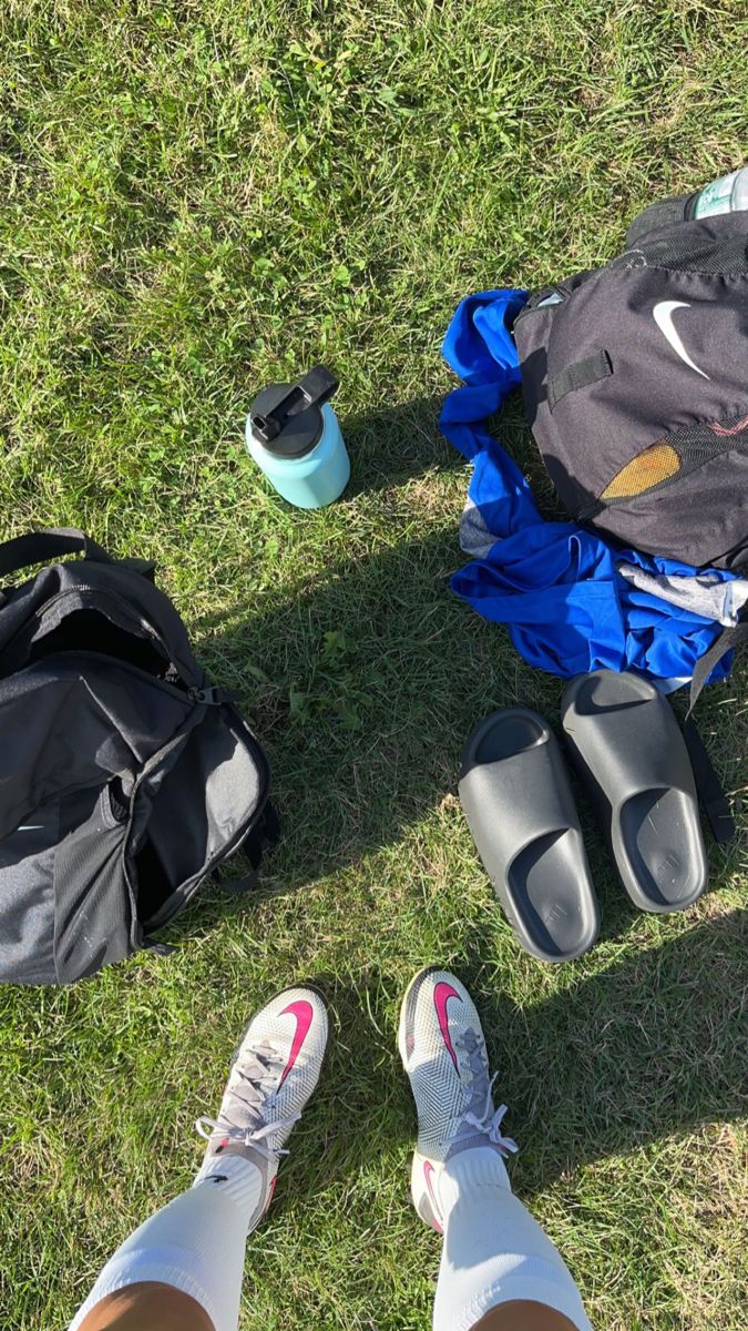 a person standing in the grass with their feet up next to backpacks and water bottles