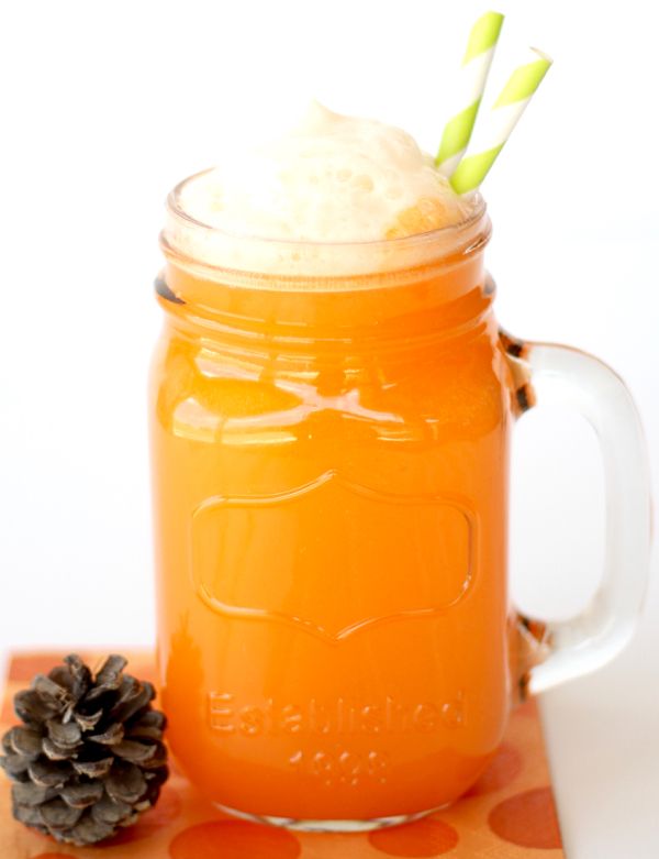 a mason jar filled with orange liquid next to a pine cone