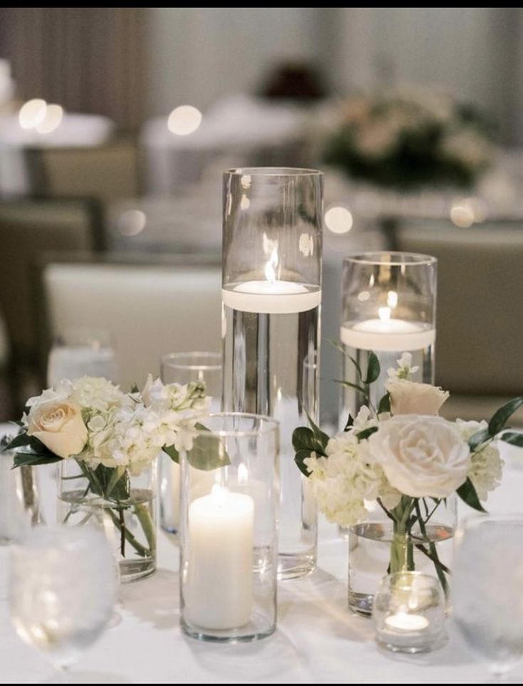 a table with candles and vases filled with white flowers on top of each other