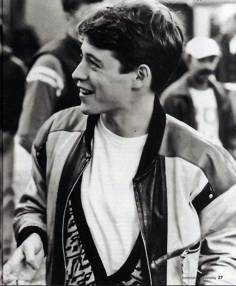 black and white photograph of a young man in a leather jacket smiling at someone behind him