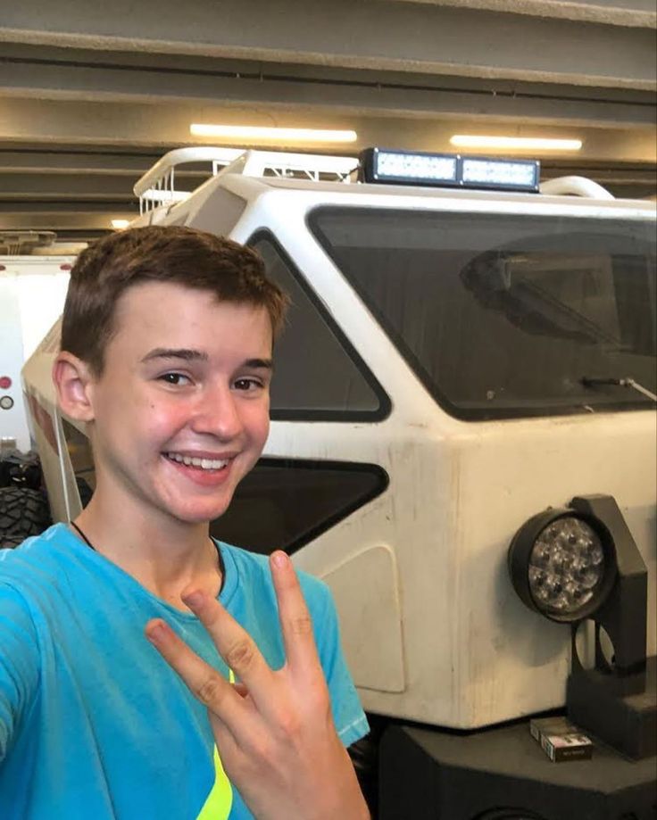 a young man making the peace sign in front of a vehicle