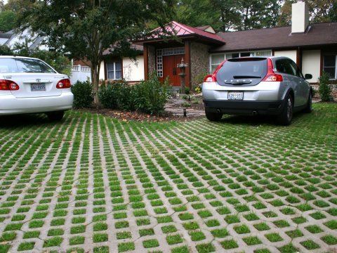 two cars parked in front of a house with grass growing on the driveway and lawn