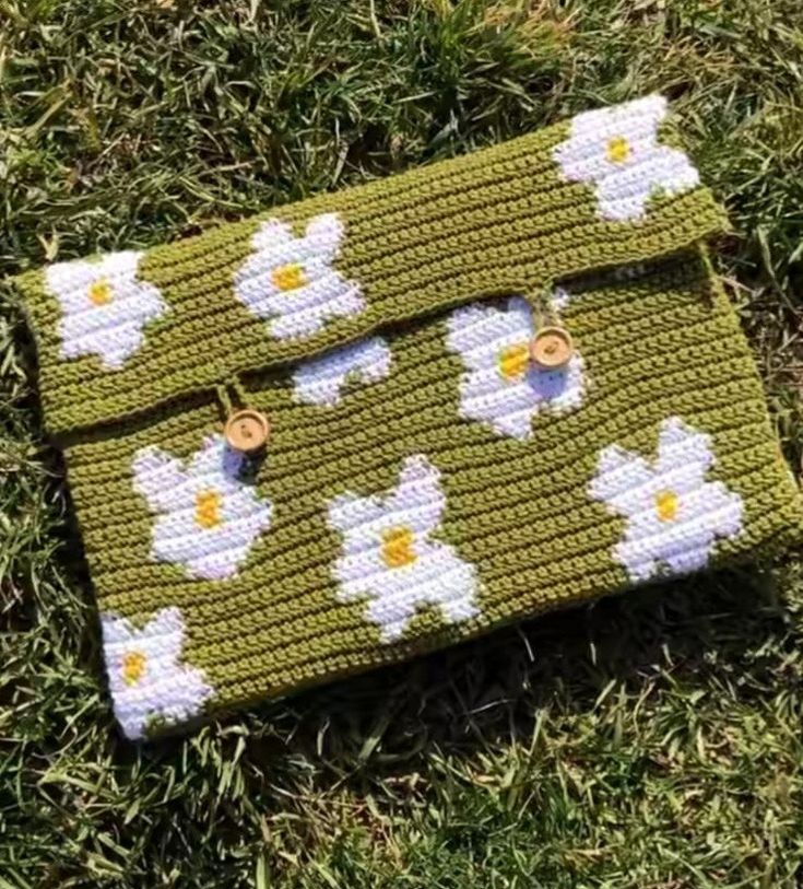 a green purse with white flowers on it sitting in the grass next to some grass