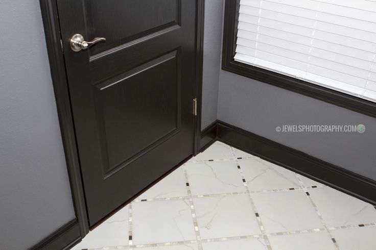 a black door is open in the corner of a room with white tile flooring