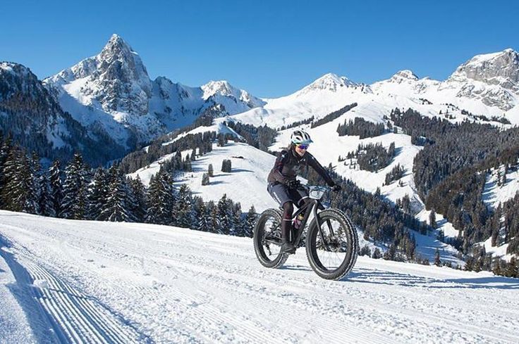 a man riding a bike down a snow covered mountain side road with mountains in the background