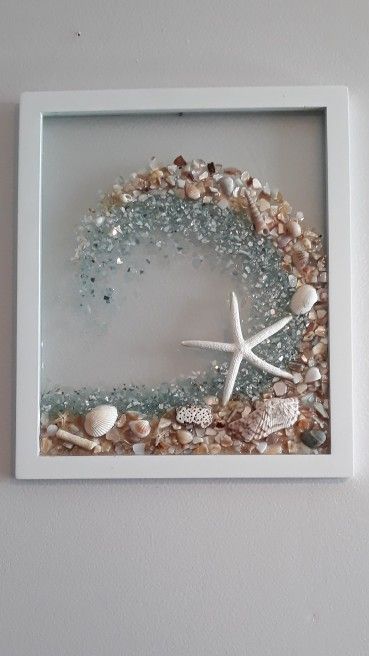 there is a glass frame with shells and starfishs in the sand on it