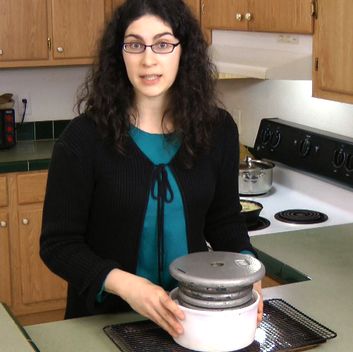 a woman standing in a kitchen holding a canister with the lid open and looking at the camera