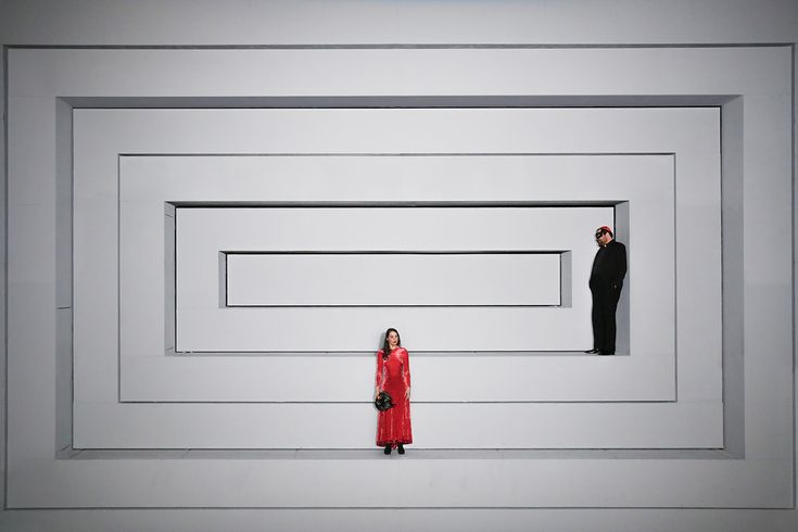 two people standing next to each other in front of a white wall with squares and rectangles