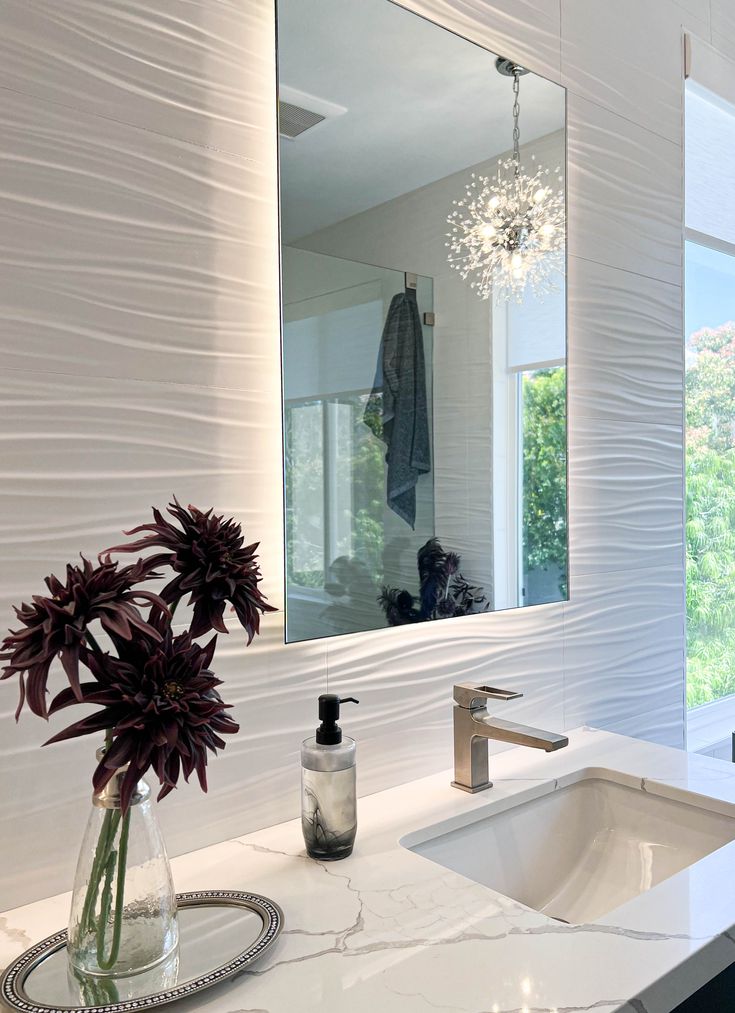 a bathroom with a large mirror above the sink and a vase with flowers in it