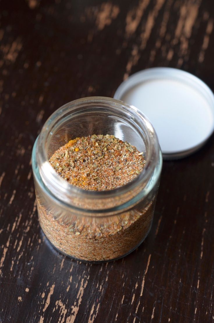 a glass jar filled with spices sitting on top of a wooden table