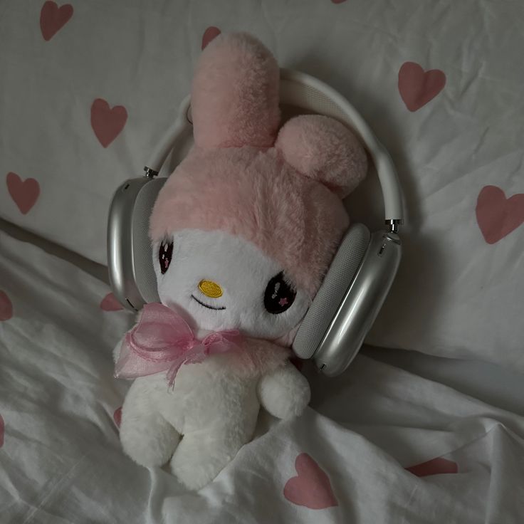 a pink and white stuffed animal with headphones on it's ears sitting on a bed