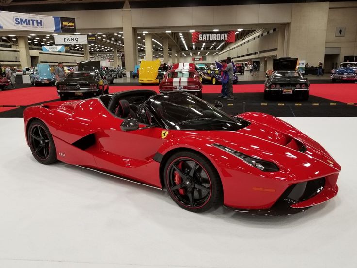 a red sports car is on display in a showroom with other cars and people