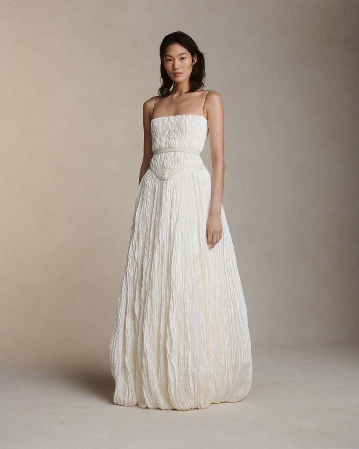 a woman in a white dress standing on a beige background with her hands behind her back